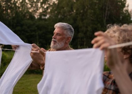 Elderly man and teenage boy working together, hanging laundry in a green outdoor setting.