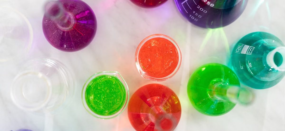 Aerial view of colorful liquids in laboratory glassware on marble surface, showcasing vibrant hues.