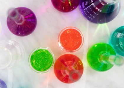 Aerial view of colorful liquids in laboratory glassware on marble surface, showcasing vibrant hues.
