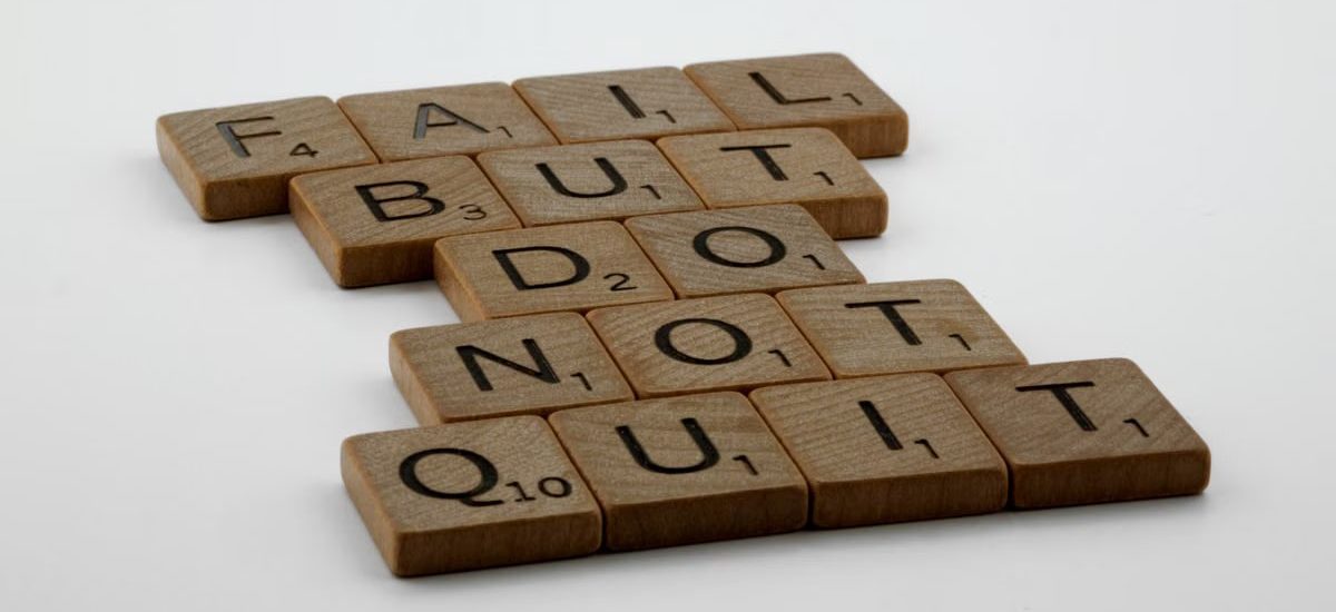 Wooden Scrabble tiles arranged to spell 'Fail but do not quit,' inspiring determination.