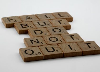 Wooden Scrabble tiles arranged to spell 'Fail but do not quit,' inspiring determination.